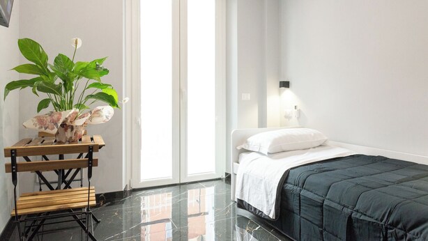 Une chambre à coucher avec un lit, une table de chevet, une plante en pot et une fenêtre avec des stores.