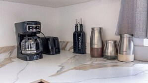 En köksbänk med en kaffebryggare, två svarta flaskor märkta med texten ”ÄTTIKA”, en behållare i rostfritt stål och en metallkanna.