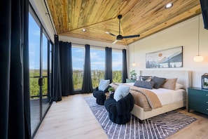 Ein Schlafzimmer mit einem großen Bett, einem Deckenventilator, einem Nachttisch, einem Gemälde und Blick durch das Fenster.