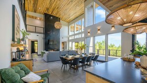 Una cocina moderna con una isla grande, comedor con mesa redonda y un rincón de estar acogedor con sofá verde.