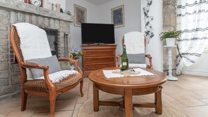 Una sala de estar con chimenea, televisor, una mesa redonda de madera y dos sillones.