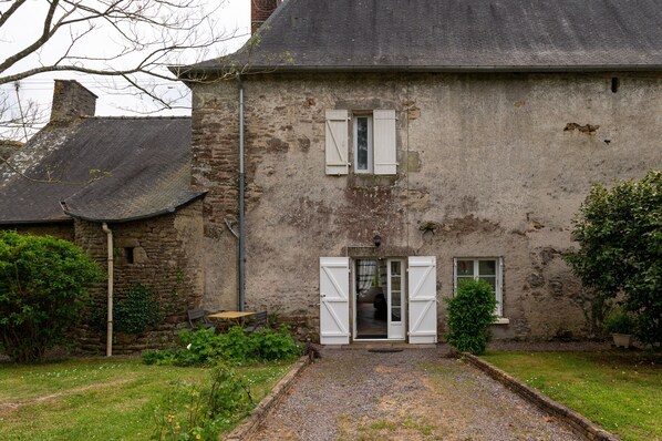 A rustic stone building with a gravel driveway, a wooden bench, and a small garden area.
