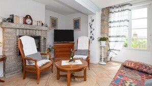 Una sala de estar con chimenea, dos sillones, un sofá, un televisor y un ventanal grande.