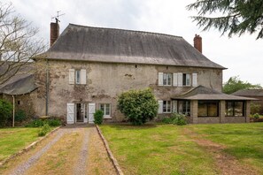Une maison à deux étages avec une allée en gravier, un petit jardin et un grand arbuste devant.