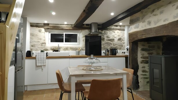 Una cocina con pared de piedra, vigas de madera, una mesa de comedor con sillas y un horno empotrado.
