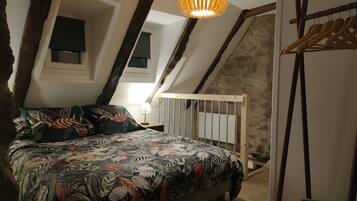 Een slaapkamer in loftstijl met een schuine kap, een bed met beddengoed met een patroon, een hanglamp en een houten kapstok.