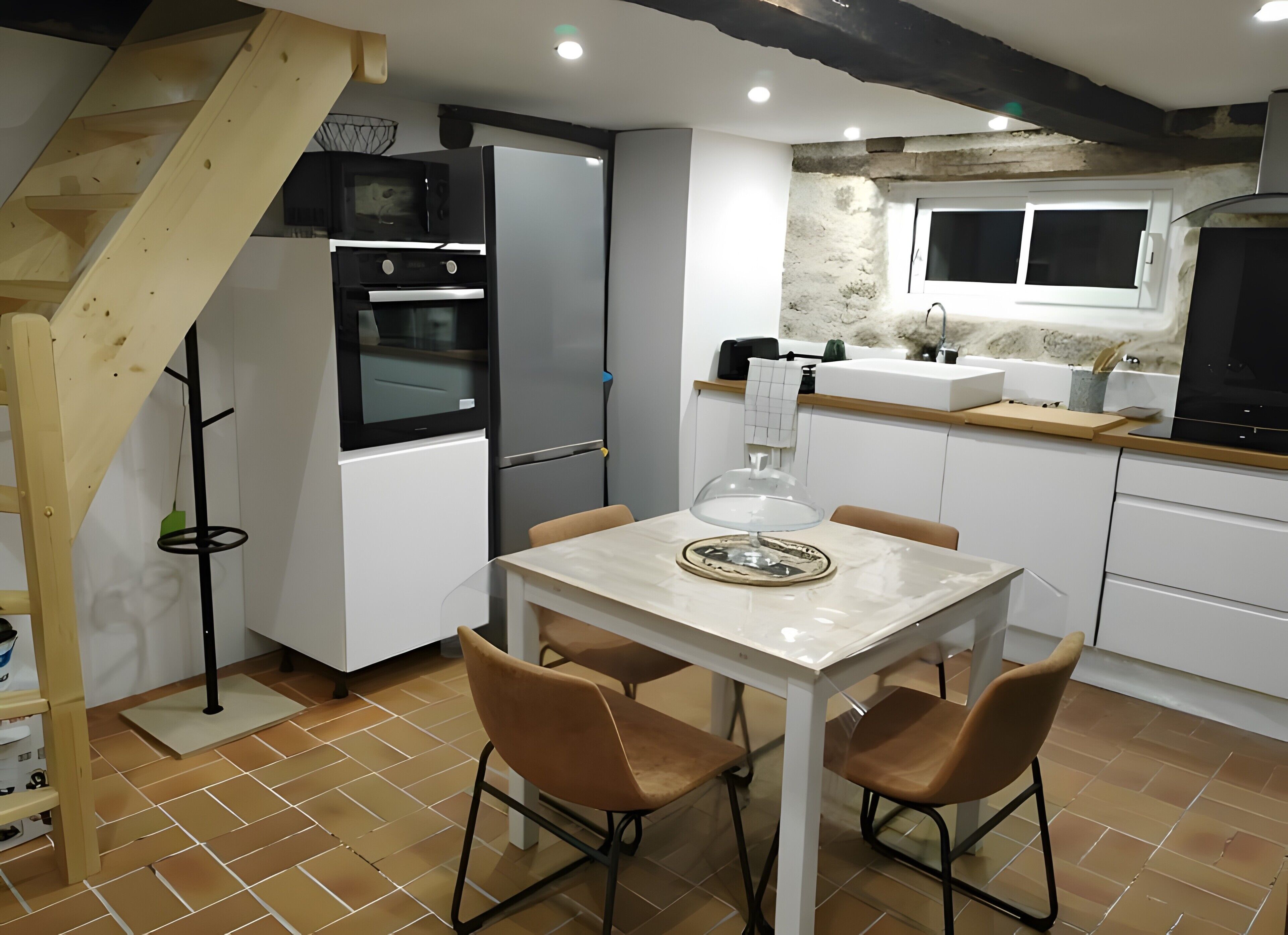 A compact kitchen with a dining area, featuring a wooden staircase, a built-in oven, a refrigerator, and a sink.