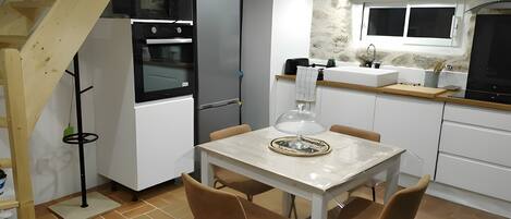 A compact kitchen with a dining area, featuring a wooden staircase, a built-in oven, a refrigerator, and a sink.