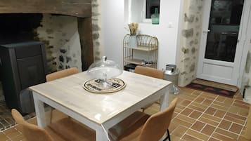 Ein Esstisch mit Stühlen, eine dekorative Glasabdeckung, ein an der Wand befestigtes Regal mit einer Vase und ein gefliester Boden.