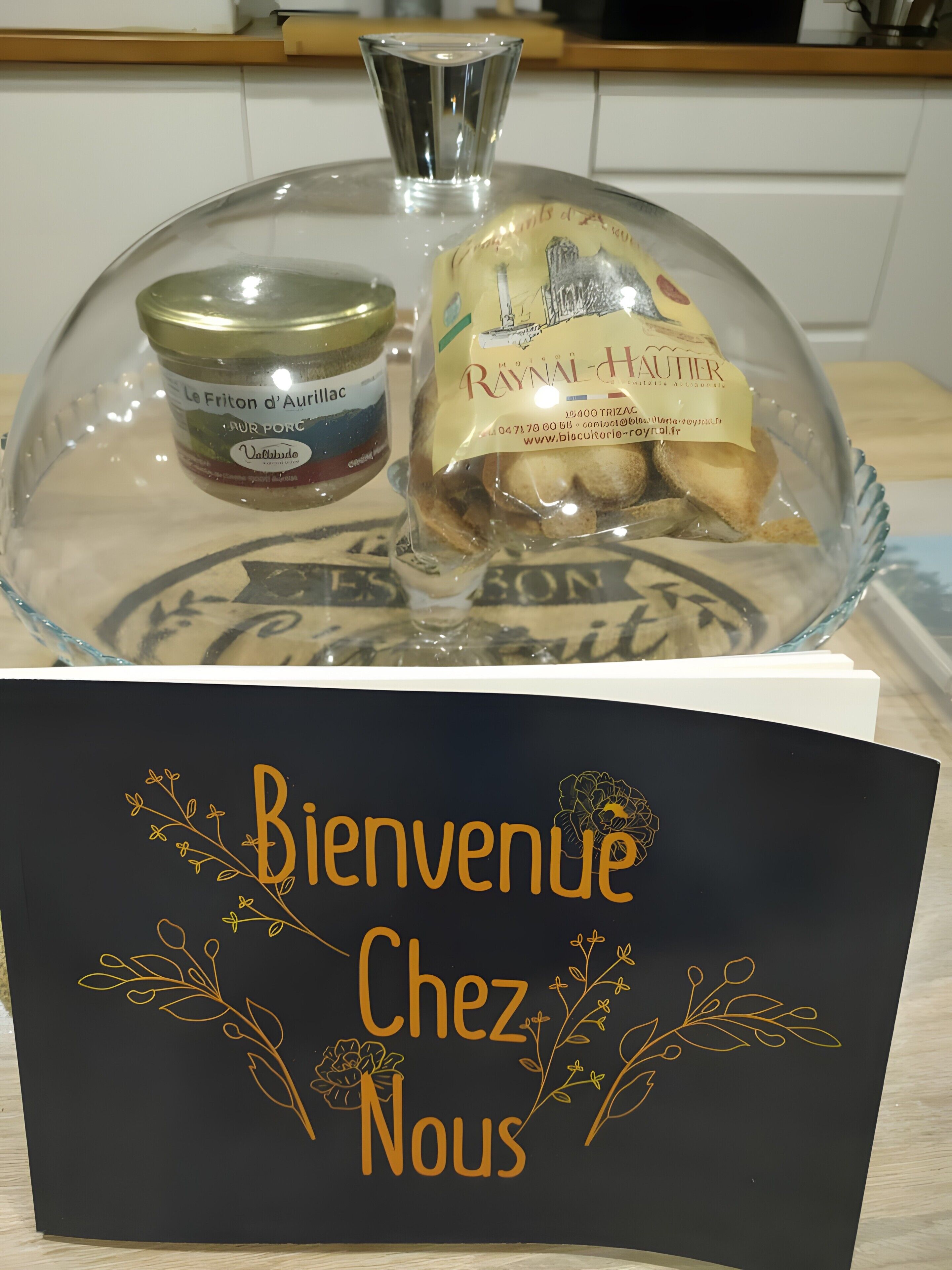 Une vitrine en verre sur laquelle est apposée une pancarte « Bienvenue chez nous », et qui contient des pots de produits « Le Friton d’Aurillac » et « Raynal Hautier ».