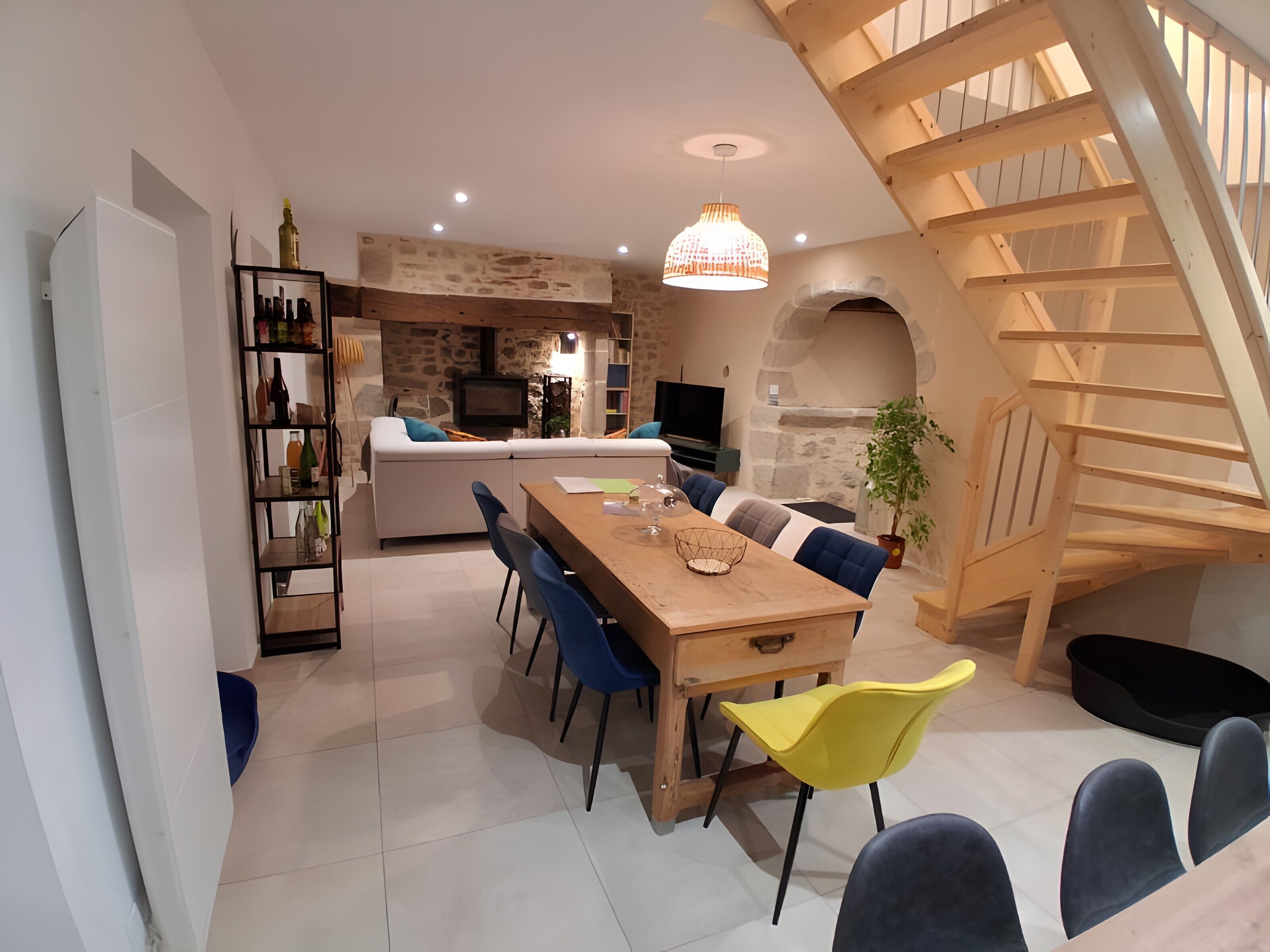 A modern kitchen with a stone wall, a wooden staircase, and a dining area with a wooden table and chairs.