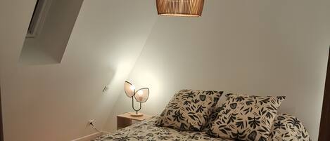 A bedroom with a bed, a hanging light fixture, a bedside table, and a window.