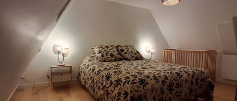A bedroom with a sloped ceiling, a bed with a leaf-patterned bedspread, a bedside lamp, and a hanging light fixture.