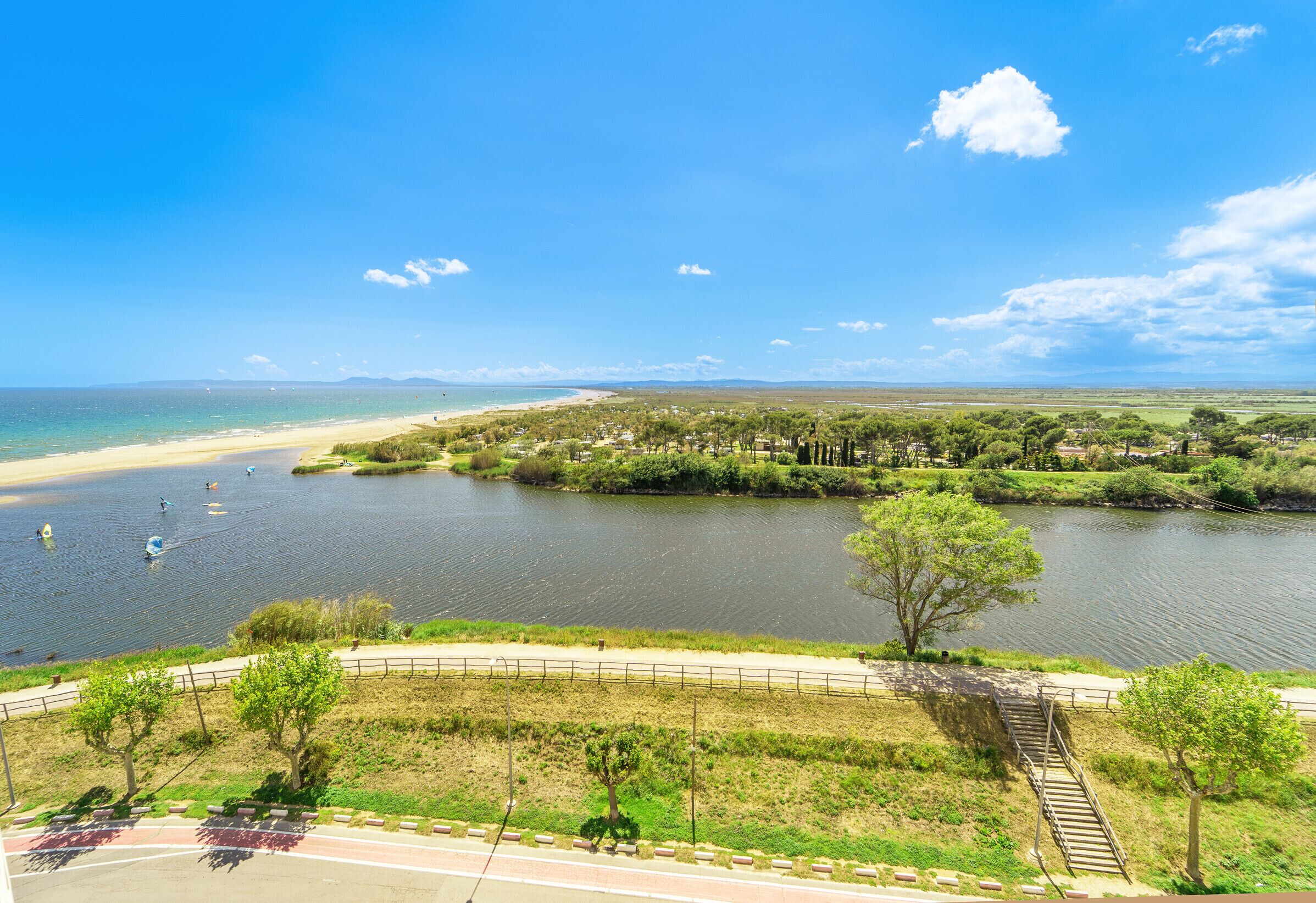 A riverside view with a beach, walking path, and greenery.