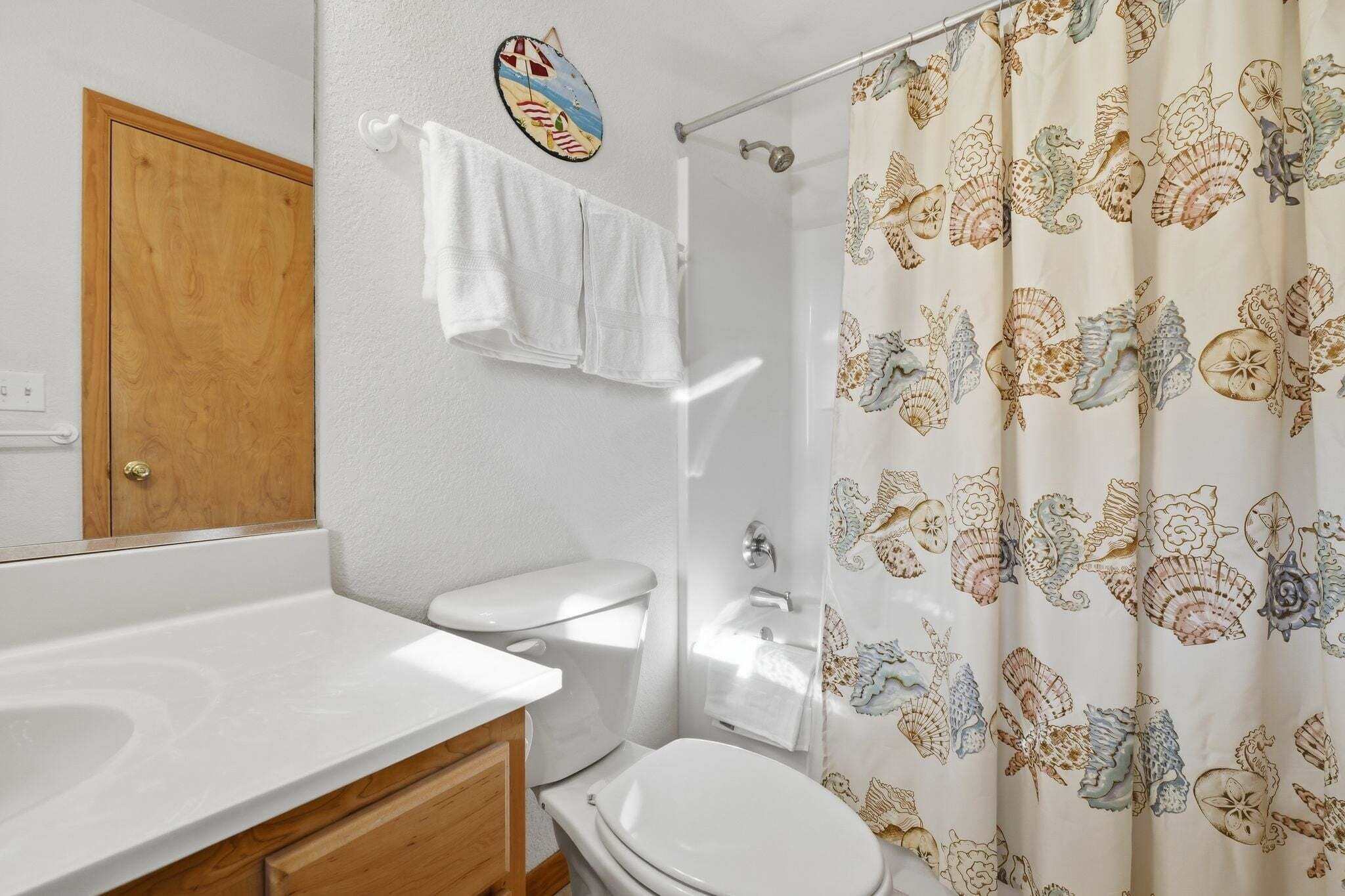 Une salle de bain avec une porte en bois, des toilettes blanches et un rideau de douche orné d’un motif représentant des hippocampes.