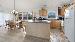 A modern kitchen with wooden cabinets, a central island, and a dining area with chairs. - Golf & Surf 7BR: Private Pool, 5 Min to Beach (Corolla)