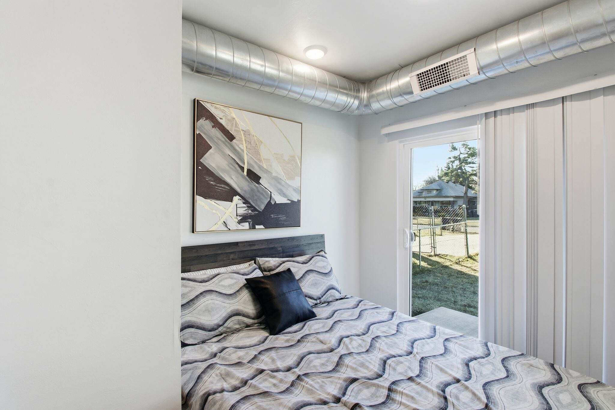 A bedroom with a bed, a large window, and a view of the outdoors.
