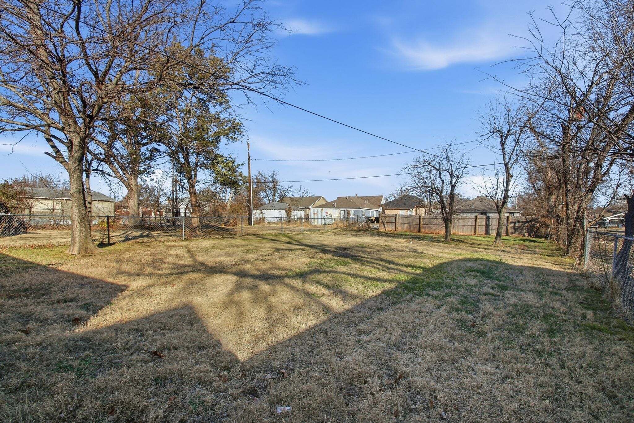 A fenced backyard with bare trees, a grassy area, and houses in the background.
