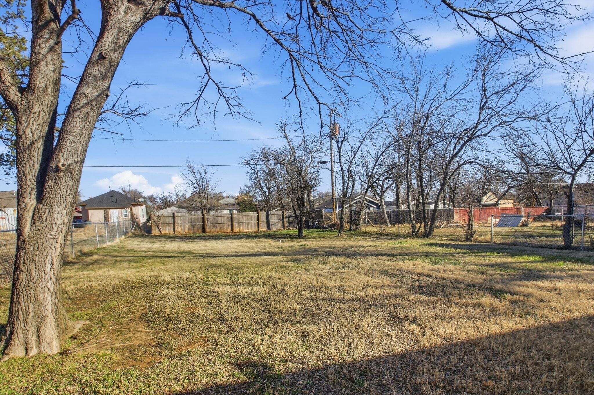 A fenced yard with trees and a clear sky.