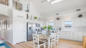 A spacious kitchen with white cabinetry, a wooden dining table, and a view to the outside. - Buho Vista 2 Bedroom Home (Port Bolivar)