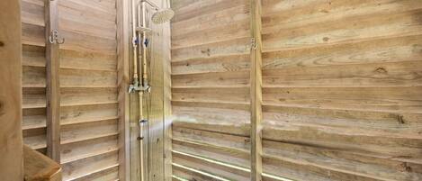 A wooden interior with a shower area, visible plumbing, and a window allowing natural light.