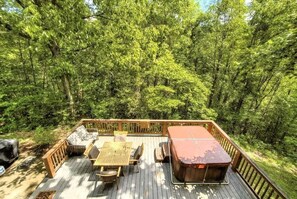 A wooden deck with outdoor furniture and a hot tub surrounded by dense green trees. - Wandering Bear Lodge 4 Bedroom Cabin (Sevierville)