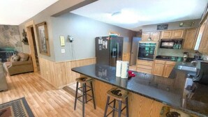 A modern kitchen with wooden cabinets, a black countertop, and two stools. - Wandering Bear Lodge 4 Bedroom Cabin (Sevierville)