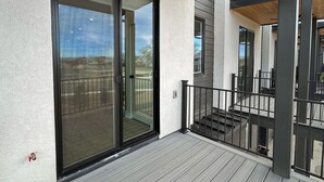 A modern building exterior with a wooden deck, a glass door, and a metal railing. - Terrace At Two Rivers 3 Bedroom Townhouse (Grand Junction)