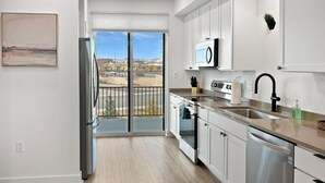 A modern kitchen with white cabinets, stainless steel appliances, and a view of a mountainous landscape through the sliding glass door. - Terrace At Two Rivers 3 Bedroom Townhouse (Grand Junction)