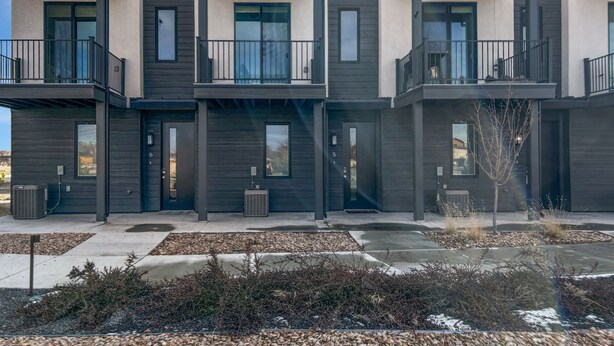 A modern multi-story residential building with balconies, large windows, and a well-maintained outdoor area with gravel and shrubs. - Terrace At Two Rivers 3 Bedroom Townhouse (Grand Junction)