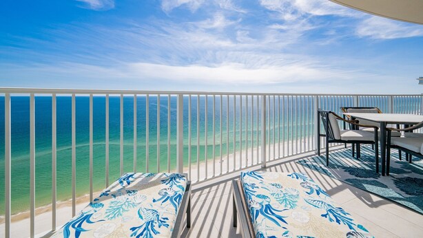 A balcony with a view of the ocean, a table, and two cushioned seating areas. - Phoenix Gulf Shores Ii 1904 3 Bedroom Condo (Gulf Shores)