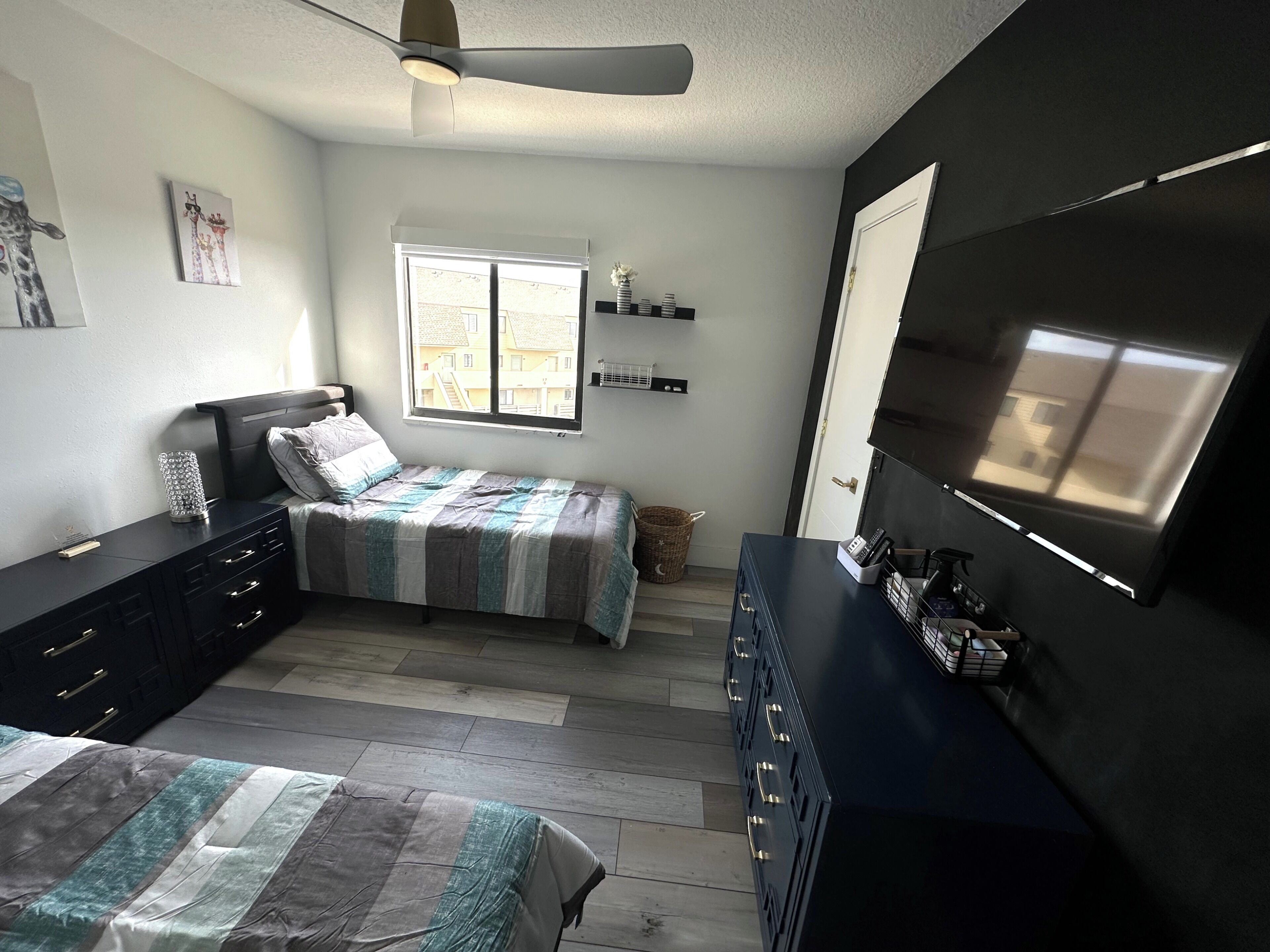 Un dormitorio con cama, cómoda, televisor y ventana con persianas.