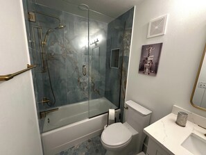 Een badkamer met een douchecabine, een toilet en een wastafel met een marmeren aanrecht.
