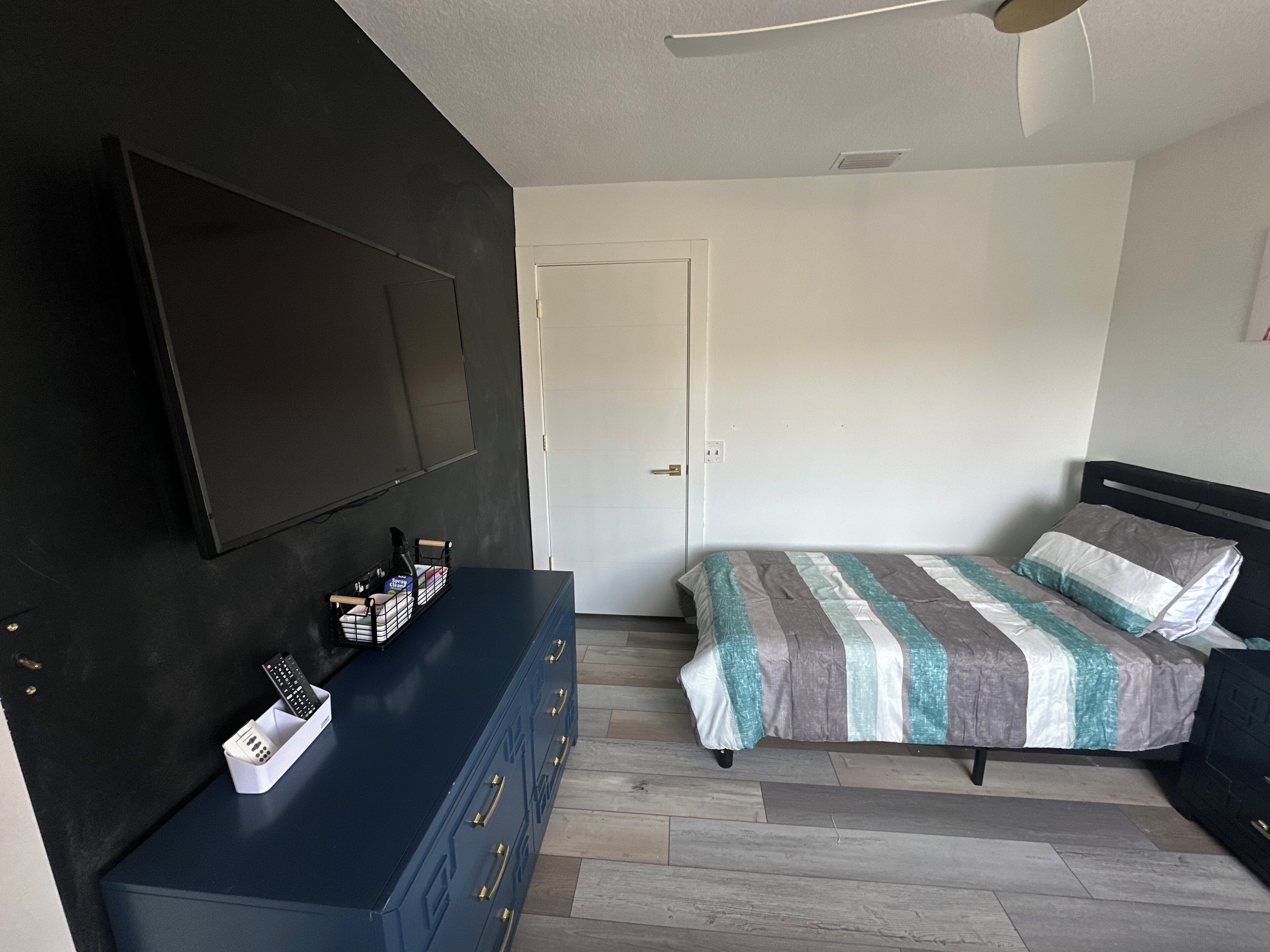 A bedroom with a bed, a dresser, a television mounted on the wall, and a door.