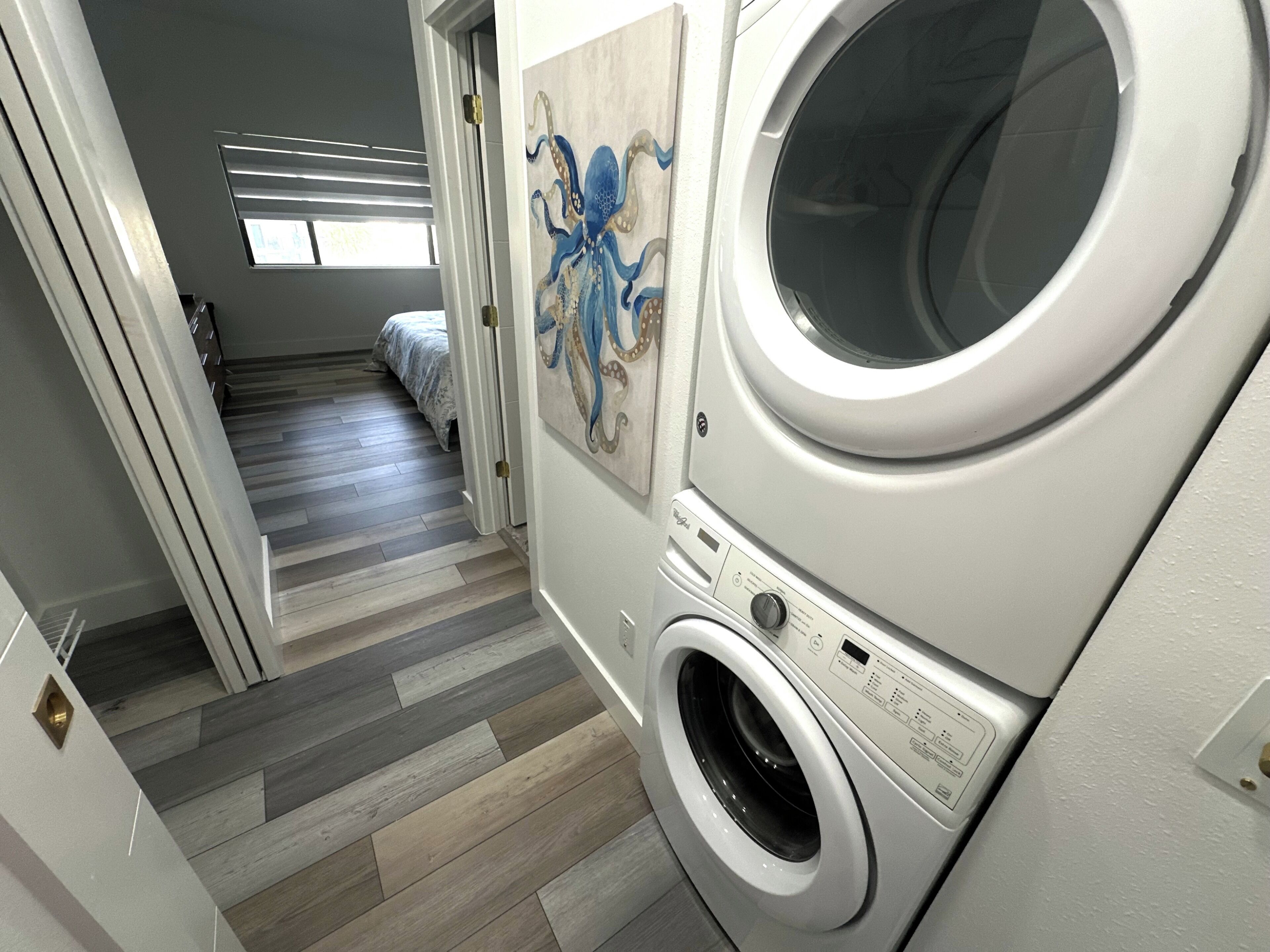 A laundry room with a front-loading washer and dryer, a wooden floor, and a painting of an octopus on the wall.