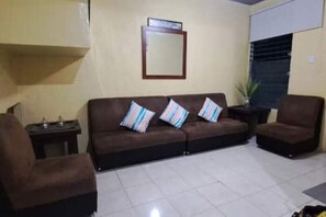 Una sala de estar con un sofá marrón, dos sillones, una mesita y una planta en maceta.