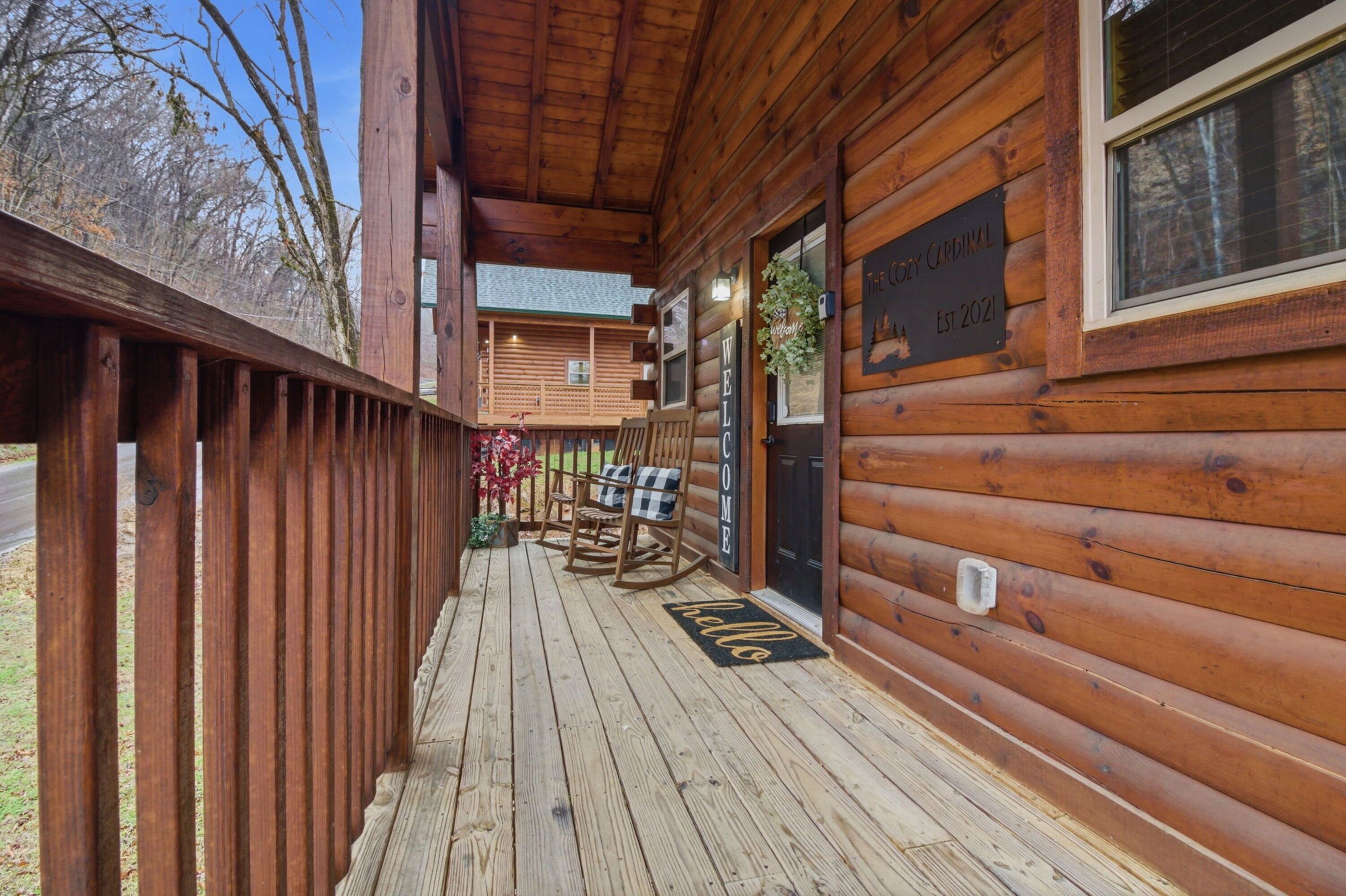 En træhytte med veranda, gyngestol og velkomst måtte.