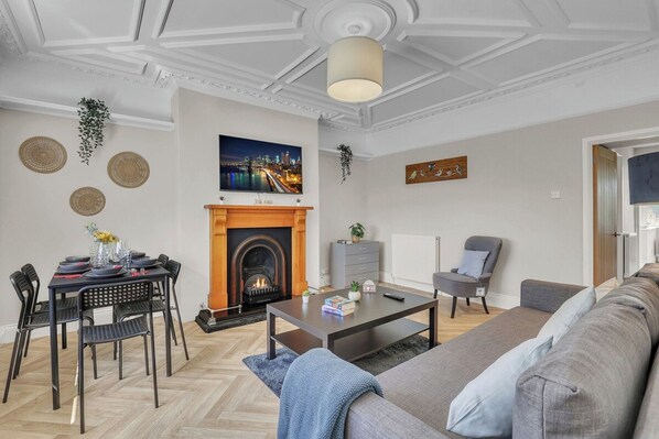 A living room with a fireplace, a television, a sofa, and a dining area with chairs and a table.