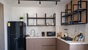 A modern kitchen with a black refrigerator, a microwave, a gas stove, and a coffee maker. There are wooden cabinets and a marble backsplash. - Apartaestudio Shanty Tipo 1 (Barranquilla)
