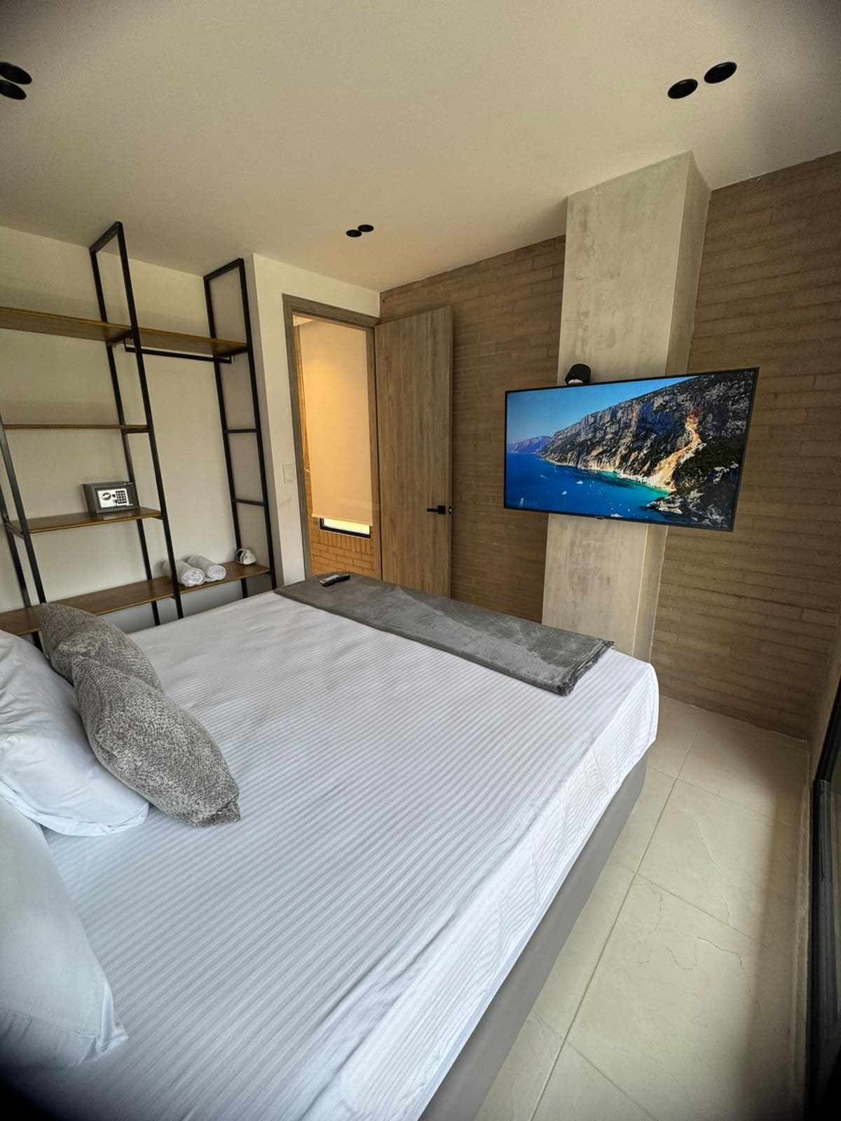 Un dormitorio moderno con cama, televisor montado en la pared y armario de madera.