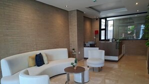 A modern lobby with a curved white sofa, a round coffee table, and a reception desk. - Apartaestudio Shanty Tipo 1 (Barranquilla)
