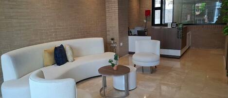A modern lobby with a curved white sofa, a round coffee table, and a reception desk.