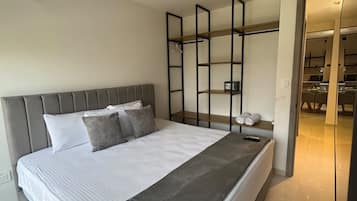 A modern bedroom with a large bed, a bedside table, a wardrobe, and a mirror.