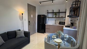 Una sala de estar moderna con una mesa de comedor de vidrio, un sofá y una cocina al fondo.