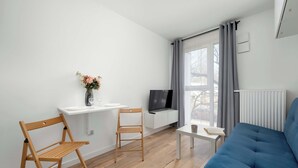 Un soggiorno moderno con un divano blu, sedie in legno, un tavolino bianco, una TV e una finestra con tende.