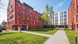 Un edificio moderno con facciate rosse e bianche, un vialetto lastricato e prati verdi.