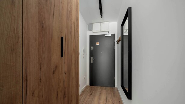 Un corridoio con una porta in legno, una porta nera e uno specchio appeso al muro.
