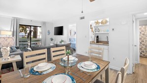 Un salon moderne avec une table à manger pour deux personnes, un ventilateur de plafond et un coin cuisine agrémenté d’objets décoratifs.