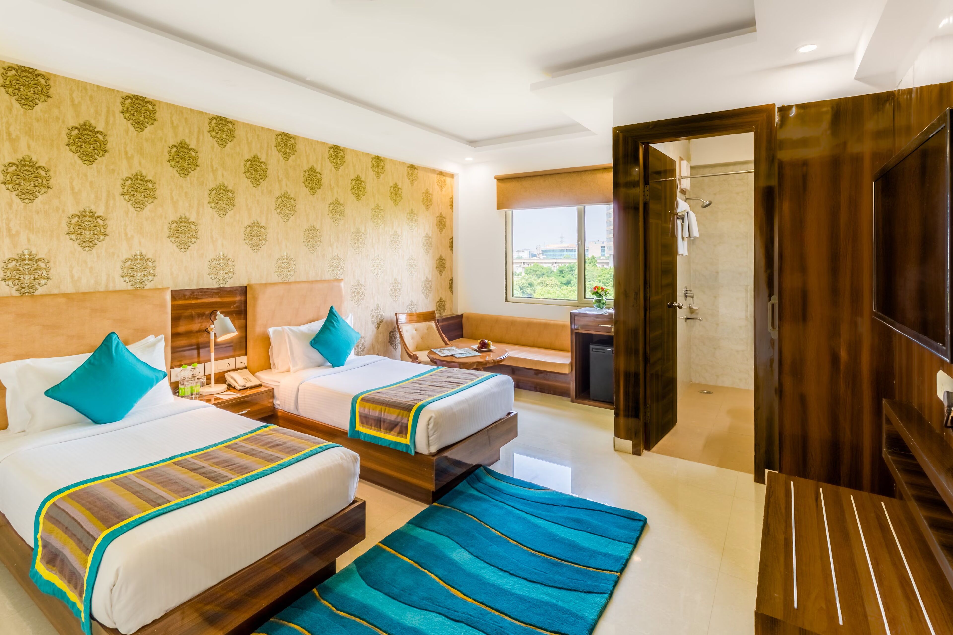 A hotel room with two beds, a desk, a chair, a small table, a window, and a door leading to a bathroom.