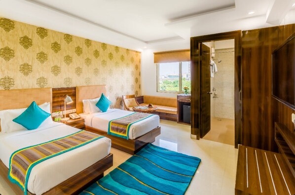A hotel room with two beds, a sofa, a TV, and a bathroom visible through an open door. - OPO Horizon LYRO, Formerly known as Inde Hotel (Gurugram)